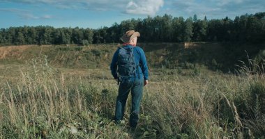 Gün batımında büyük bir kum ocağında elinde sırt çantasıyla duran kovboy şapkalı bir yürüyüşçü.