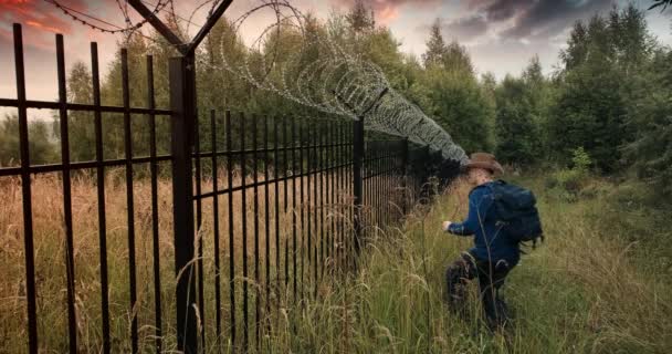 Adam dikenli tellerle çitlere doğru koşuyor ve üzerine tırmanıyor. Akşam batımı — Stok video
