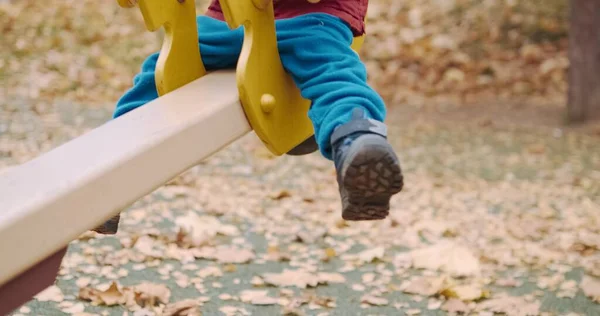 Ein kleines, niedliches Kind reitet auf einer Schaukel im Hof bei einem Spaziergang. Beine aus nächster Nähe — Stockfoto