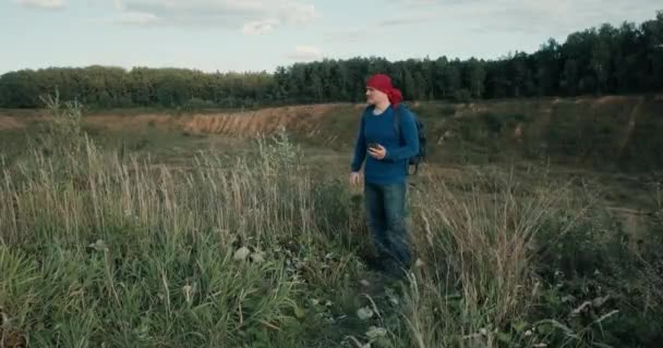 Caminatas con mochila y teléfono móvil en una cantera grande y arenosa al atardecer — Vídeos de Stock