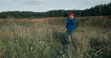 Yürüyüşçü gün batımında büyük, kumlu taş ocağında sırt çantası ve cep telefonuyla yürüyor.