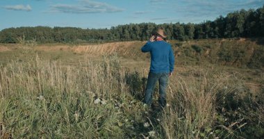 Kovboy şapkalı bir yürüyüşçü, gün batımında kum ocağı. Bir adam telefonda konuşuyor.