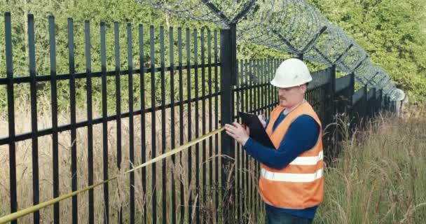 Worker with a measuring tape measure a fence with barbed wire — Stock Video