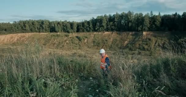 Ingeniero de trabajo en un casco blanco junto a una fosa de arena. El hombre está muy cansado. — Vídeo de stock