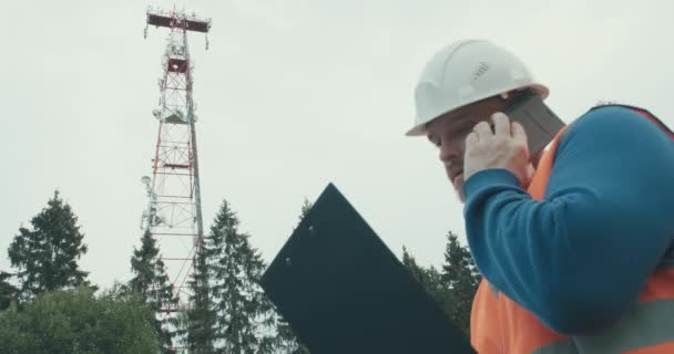 Obok stoi komórkowa wieża radiowa 4G 5G, pracownik w kombinezonie i hełmie — Wideo stockowe