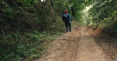 Kırmızı bandanalı bir yürüyüşçü yaz ormanının ortasında dik bir yamaçta yürür.