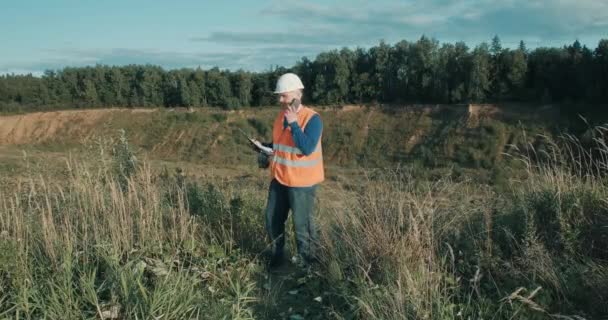 Ingeniero de trabajo en casco blanco junto a una fosa de arena. Foreman está hablando por teléfono. — Vídeos de Stock