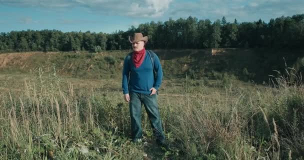 Wędrowiec w kowbojskim kapeluszu chodzi z plecakiem w dużym kamieniołomie piasku o zachodzie słońca — Wideo stockowe