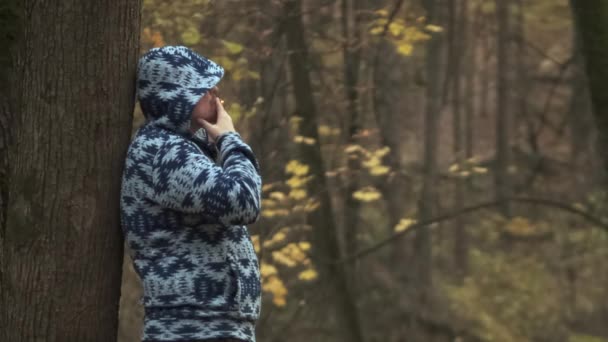 Retrato de un hombre triste fumando un cigarrillo en el bosque de otoño apoyado en un árbol — Vídeos de Stock