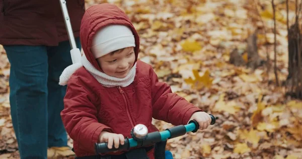 Mom rides cute little girl on bicycle in autumn park. Cool weather — Stock Photo, Image