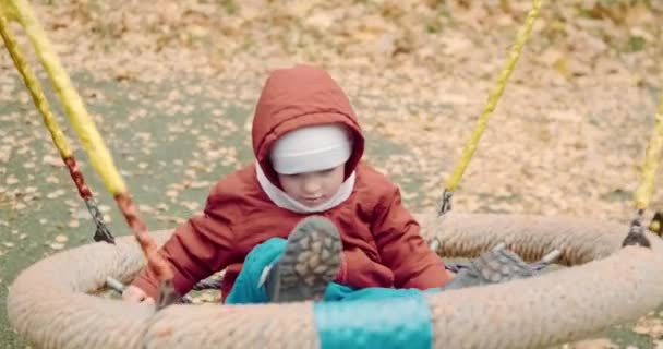 Pequeño, lindo niño paseos en un columpio en el patio en un paseo con sus padres — Vídeos de Stock