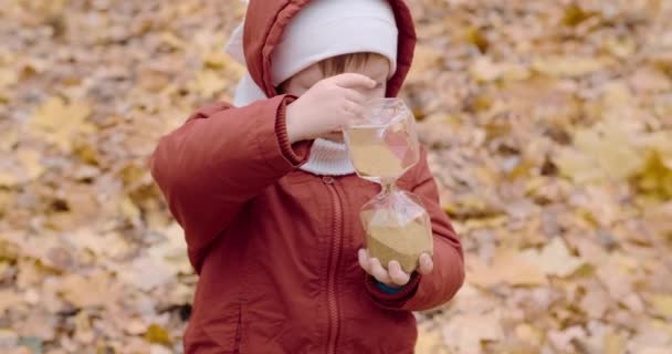 Little, una ragazza caucasica sta giocando con una clessidra di vetro nella foresta autunnale — Video Stock