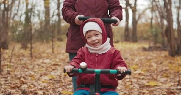 Mãe monta bonito menina na bicicleta no parque de outono. Tempo frio — Vídeo de Stock