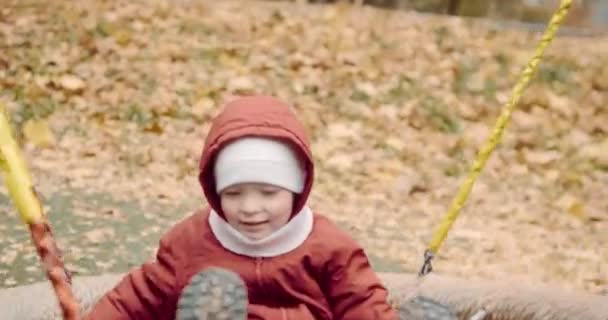 Pequeño, lindo niño paseos en un columpio en el patio en un paseo con sus padres — Vídeos de Stock