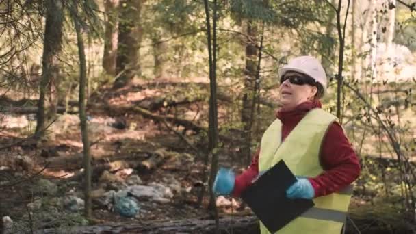 Ekolog kvinna i arbetskläder dansar mot bakgrund av skräp i skogen — Stockvideo