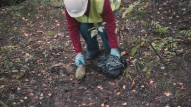 İş kıyafetleri ve kask giyen çevre bilimci kadın ormandaki çöpleri temizliyor.