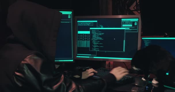 Hacker in un cappuccio siede di fronte a schermi di computer e database di hack — Video Stock