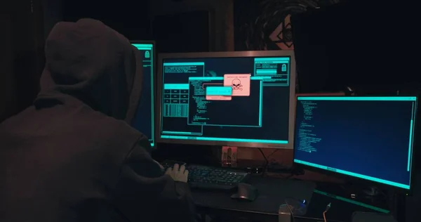 Hacker en una capucha se sienta frente a las pantallas de la computadora y hacks bases de datos Fotos de stock libres de derechos