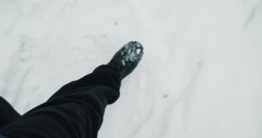 Soğuk kışta, karda yürürken botları olan bir adamın ayakları.