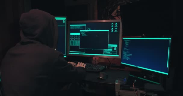 Hacker in un cappuccio siede di fronte a schermi di computer e database di hack — Video Stock