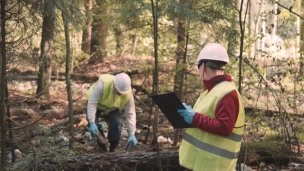 Еколог людина в робочому одязі і шоломі чистий пластиковий сміття в лісі — стокове відео