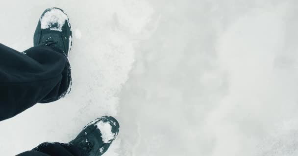 Los pies del hombre en las botas que caminan sobre el hielo delgado en invierno frío, el arroyo fluye bajo el hielo — Vídeo de stock
