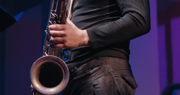 El saxofonista en un concierto toca el saxofón y baila. Está oscuro. — Vídeos de Stock