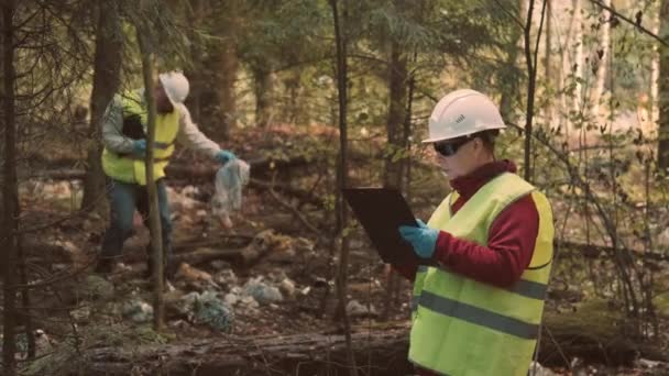 Ecologista homem em vestuário de trabalho e capacete lixo plástico limpo na floresta — Vídeo de Stock