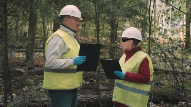 Άνδρας και γυναίκα οικολόγος σε ενδύματα εργασίας με φόντο τα σκουπίδια στο δάσος — Αρχείο Βίντεο