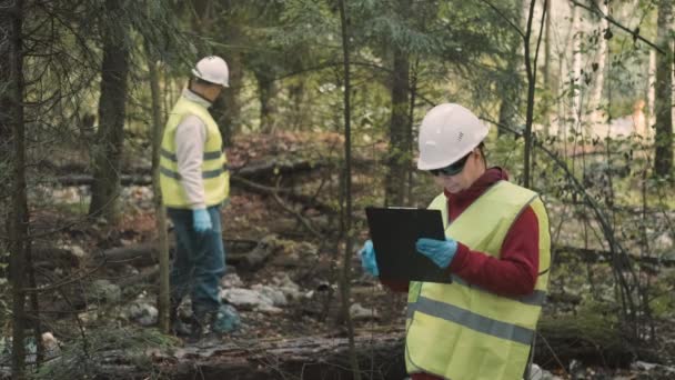 Ekolog man i arbetskläder och hjälm samlar plast skräp i skogen — Stockvideo