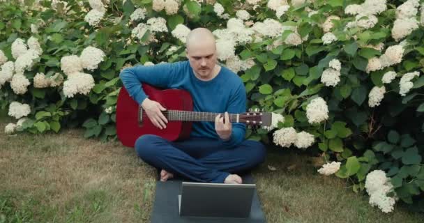 El hombre está en la naturaleza y los profesores en línea lecciones de guitarra acústica — Vídeo de stock