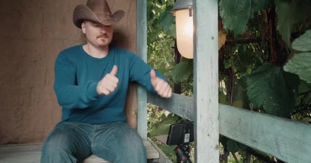 Cowboy man communiceert online met behulp van zijn telefoon tijdens het zitten op de veranda — Stockvideo