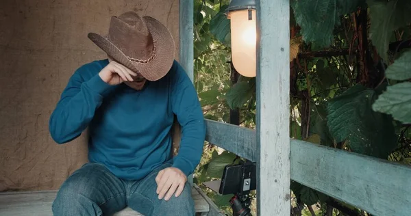 Cowboy uomo guarda commedia sul suo telefono e ride seduto sul portico di casa — Foto Stock