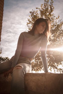 Parkta yürüyen ve kameraya bakan bir kız oturuyor ve arka planda doğa ile duruyor..