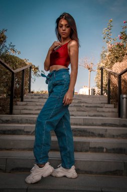 Parkta yürüyen ve kameraya bakan bir kız oturuyor ve arka planda doğa ile duruyor..