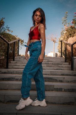 Parkta yürüyen ve kameraya bakan bir kız oturuyor ve arka planda doğa ile duruyor..