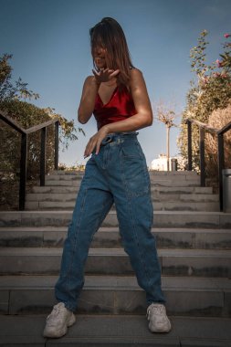 Parkta yürüyen ve kameraya bakan bir kız oturuyor ve arka planda doğa ile duruyor..