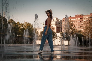 Parkta yürüyen ve kameraya bakan bir kız oturuyor ve arka planda doğa ile duruyor..