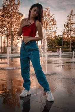 Parkta yürüyen ve kameraya bakan bir kız oturuyor ve arka planda doğa ile duruyor..