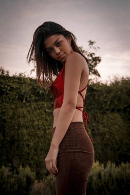 Parkta yürüyen ve kameraya bakan bir kız oturuyor ve arka planda doğa ile duruyor..