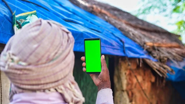 Indian old man holding a mobile phone and point towards it's screen. Mobile phone with a green screen for mockup.