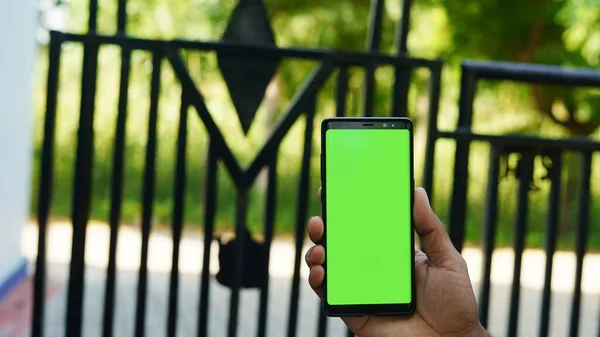 Man hand holding the smartphone with green screen isolated on the main entrance background.