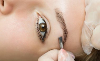 Kuaförün elleri beyaz eldivenlerle kaşlarını cımbızla alıyor. Güzel, çekici bir kadın yüzü. Güzel saçlı, bakımlı bir kadın ya da kadın. Kaş şekillendirme ve kaplama.