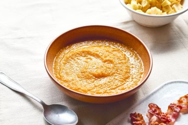 Kavrulmuş pastırmalı balkabağı kremalı çorba ve masada keten masa örtüsüyle birlikte kil tabakta kızarmış ekmek. Sonbahar sebze kremalı çorba püresi. Sağlıklı mevsimsel yemek.