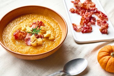 Kavrulmuş pastırmalı balkabağı kremalı çorba ve masada keten masa örtüsüyle birlikte kil tabakta kızarmış ekmek. Sonbahar sebze kremalı çorba püresi. Sağlıklı mevsimsel yemek.
