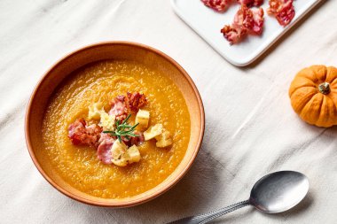 Kavrulmuş pastırmalı balkabağı kremalı çorba ve masada keten masa örtüsüyle birlikte kil tabakta kızarmış ekmek. Sonbahar sebze kremalı çorba püresi. Sağlıklı mevsimsel yemek.