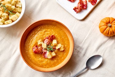 Kavrulmuş pastırmalı balkabağı kremalı çorba ve masada keten masa örtüsüyle birlikte kil tabakta kızarmış ekmek. Sonbahar sebze kremalı çorba püresi. Sağlıklı mevsimsel yemek.
