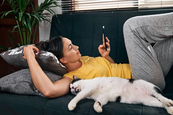 Brunetka Leżąca Kotem Kanapie Używa Telefonu Komórkowego Ludzie Gadżetem Komunikacja — Zdjęcie stockowe