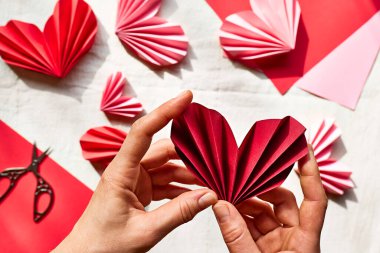 Kadın elleri kağıt kalp yapıyor. Origami çelengi. Sevgililer Günü için aşkın sembolü, mutlu yıllar, anneler günü, kadınlar günü. Diy. Adım adım..