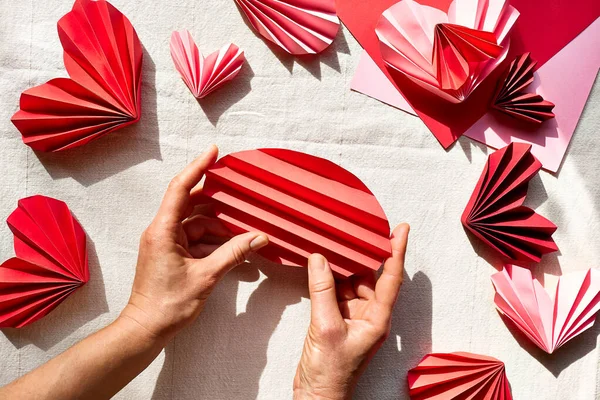 Woman hands making paper hearts. Origami garland. Symbol of love for valentines day, happy birthday, greetings, Mothers day, Women\'s day. Diy. Step by step. Step three.